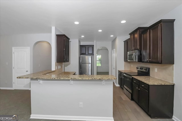 kitchen with a kitchen breakfast bar, light stone counters, kitchen peninsula, stainless steel appliances, and light wood-type flooring