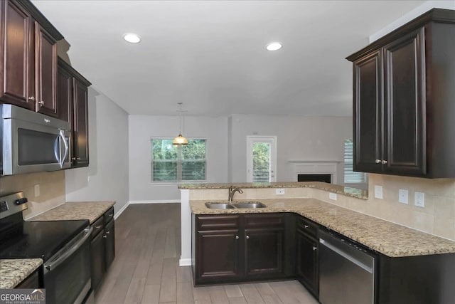 kitchen with pendant lighting, sink, kitchen peninsula, light hardwood / wood-style flooring, and appliances with stainless steel finishes