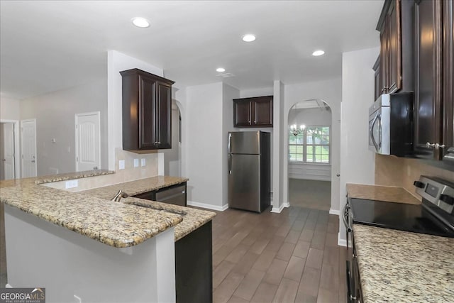 kitchen with appliances with stainless steel finishes, kitchen peninsula, light stone countertops, dark hardwood / wood-style flooring, and a breakfast bar area