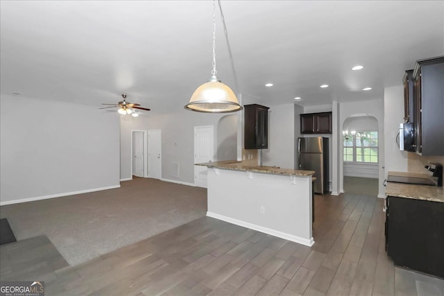 kitchen with hanging light fixtures, kitchen peninsula, dark wood-type flooring, stainless steel appliances, and light stone countertops