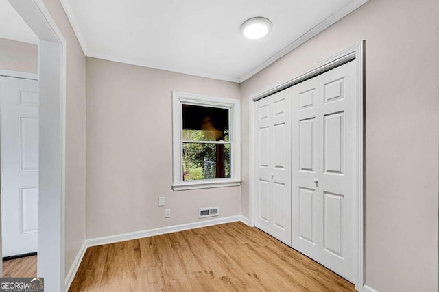 unfurnished bedroom with light wood-type flooring, a closet, and ornamental molding