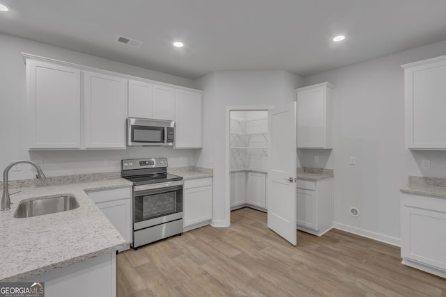 kitchen with light hardwood / wood-style floors, white cabinetry, light stone countertops, stainless steel appliances, and sink