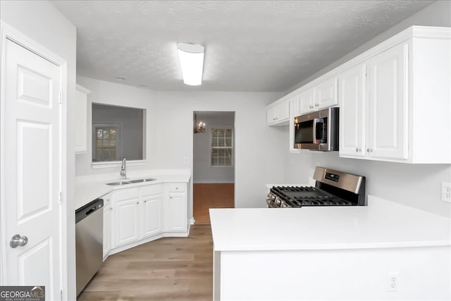 kitchen with white cabinets, stainless steel appliances, a textured ceiling, light hardwood / wood-style flooring, and sink