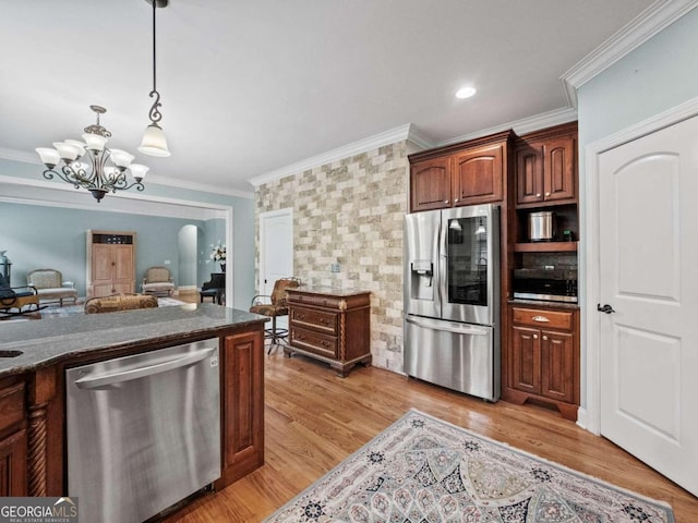 kitchen with appliances with stainless steel finishes, ornamental molding, custom exhaust hood, sink, and hanging light fixtures