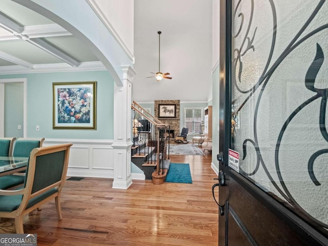 foyer featuring a towering ceiling, decorative columns, ornamental molding, ceiling fan, and light hardwood / wood-style floors