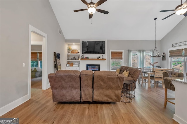 living room featuring light wood-type flooring, ceiling fan with notable chandelier, and plenty of natural light