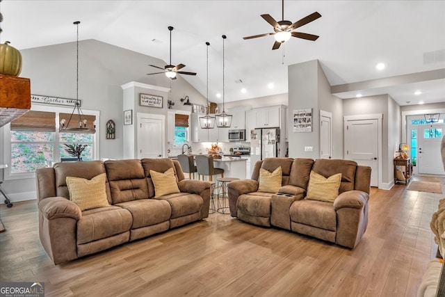 living room with ceiling fan, light wood-type flooring, and high vaulted ceiling