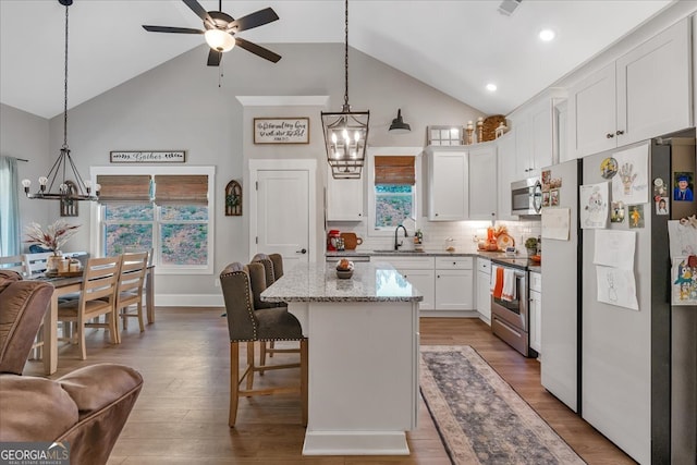 kitchen featuring appliances with stainless steel finishes, high vaulted ceiling, wood-type flooring, a kitchen bar, and a center island