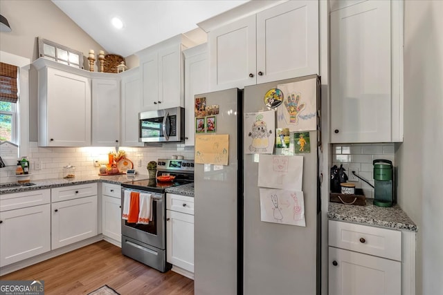 kitchen featuring white cabinetry, vaulted ceiling, light hardwood / wood-style flooring, backsplash, and appliances with stainless steel finishes