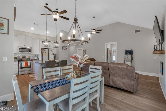 dining area with light wood-type flooring, ceiling fan with notable chandelier, and high vaulted ceiling