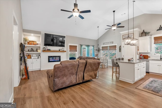 living room featuring ceiling fan with notable chandelier, light wood-type flooring, sink, and high vaulted ceiling