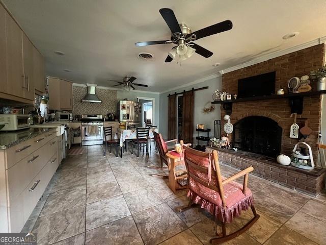 interior space with ceiling fan, stainless steel appliances, a barn door, ventilation hood, and a fireplace