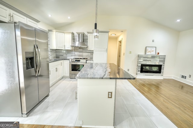 kitchen featuring pendant lighting, stainless steel appliances, lofted ceiling, dark stone counters, and wall chimney range hood