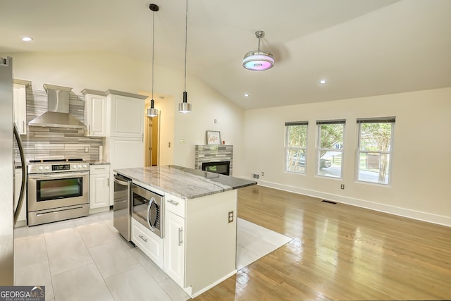 kitchen featuring light stone counters, white cabinets, wall chimney range hood, stainless steel appliances, and vaulted ceiling