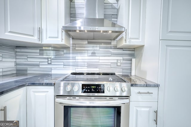 kitchen featuring stainless steel electric stove, tasteful backsplash, wall chimney range hood, and white cabinetry