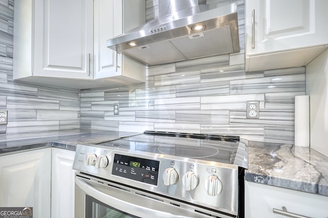 kitchen with dark stone countertops, tasteful backsplash, white cabinets, stainless steel stove, and range hood