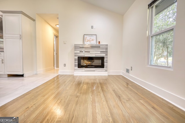 unfurnished living room with vaulted ceiling, light hardwood / wood-style floors, and a tile fireplace