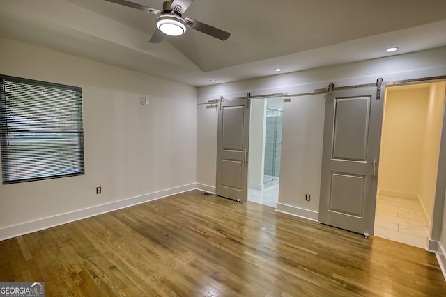 unfurnished bedroom with light hardwood / wood-style floors, ensuite bathroom, ceiling fan, and a barn door