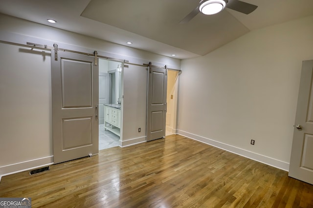 unfurnished bedroom with a barn door, connected bathroom, light wood-type flooring, and ceiling fan