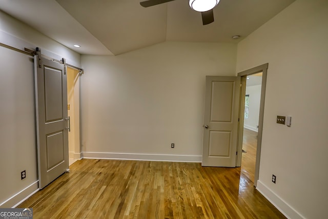 unfurnished bedroom with light hardwood / wood-style flooring, ceiling fan, and a barn door