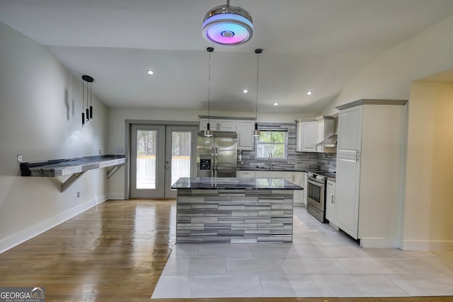 kitchen featuring sink, wall chimney range hood, stainless steel appliances, decorative light fixtures, and dark stone countertops