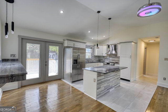 kitchen with hanging light fixtures, stainless steel fridge, white cabinets, light hardwood / wood-style flooring, and wall chimney range hood