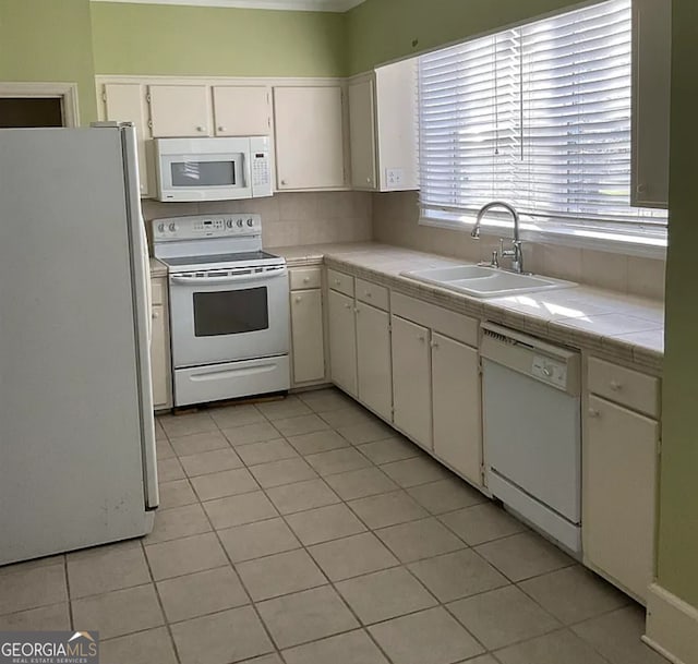 kitchen featuring white cabinets, white appliances, light tile patterned floors, tile counters, and sink