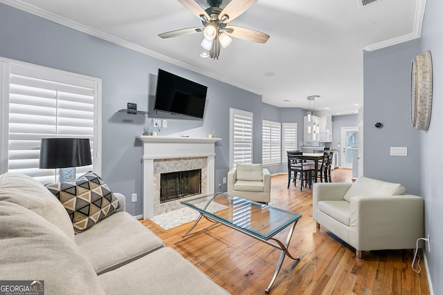 living room with light hardwood / wood-style flooring, a tiled fireplace, ceiling fan, and ornamental molding