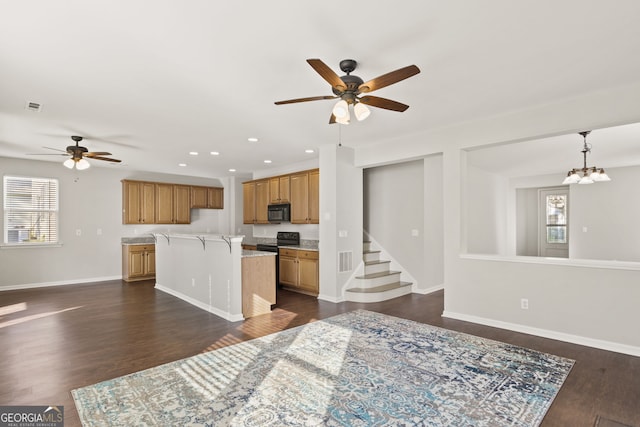 kitchen with decorative light fixtures, dark hardwood / wood-style floors, a center island, a breakfast bar area, and ceiling fan with notable chandelier