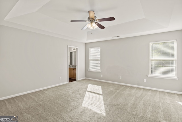 carpeted spare room featuring a raised ceiling, ceiling fan, and plenty of natural light