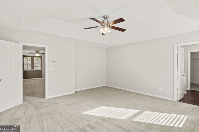 empty room featuring ceiling fan, a raised ceiling, and carpet floors