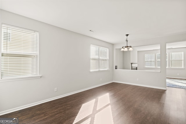 unfurnished room with a notable chandelier and dark hardwood / wood-style floors