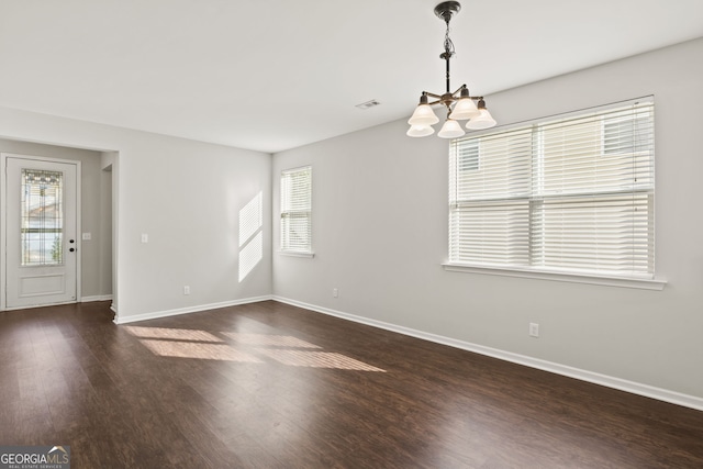 spare room with a notable chandelier and dark hardwood / wood-style floors