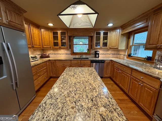 kitchen featuring decorative backsplash, light stone countertops, light hardwood / wood-style flooring, and stainless steel appliances