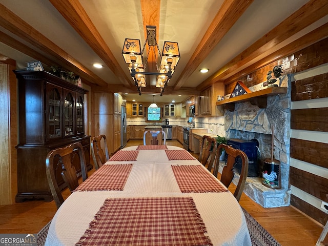 dining area featuring a stone fireplace, light hardwood / wood-style floors, and beam ceiling