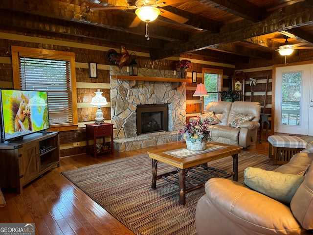 living room featuring wood-type flooring, beamed ceiling, a fireplace, wooden walls, and ceiling fan