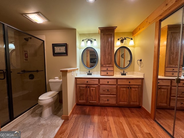 bathroom featuring wood-type flooring, a shower with door, vanity, and toilet