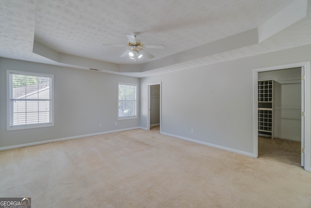 unfurnished bedroom with light carpet, a raised ceiling, ceiling fan, and a walk in closet