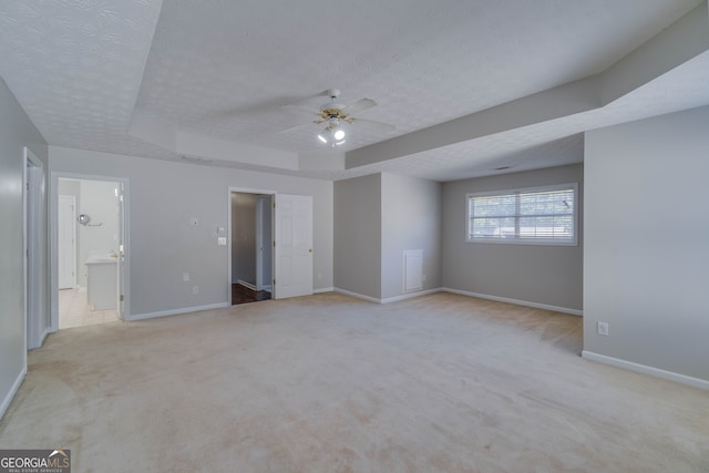 unfurnished bedroom featuring light carpet, a textured ceiling, a raised ceiling, and ceiling fan