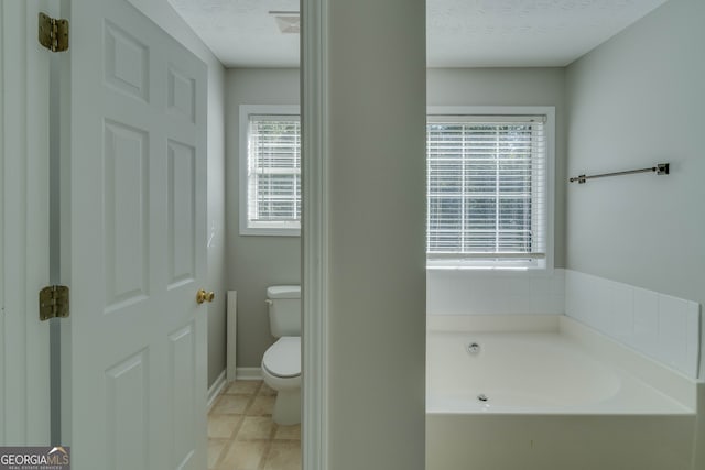 bathroom with a textured ceiling, a tub to relax in, plenty of natural light, and toilet