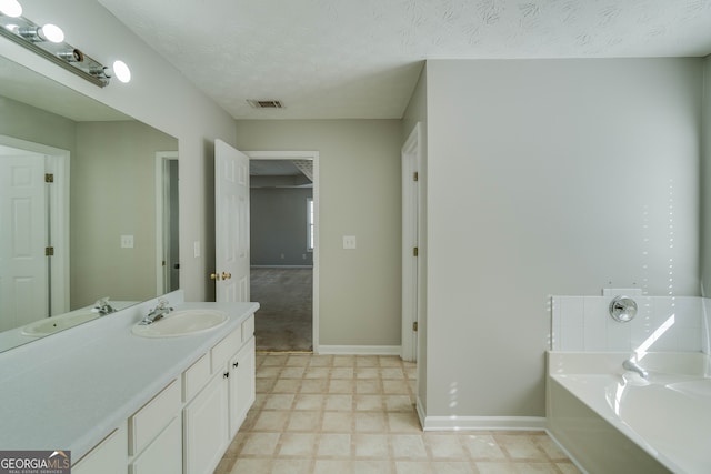 bathroom with a textured ceiling, vanity, and a washtub