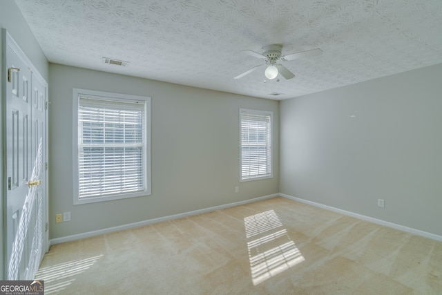 carpeted spare room featuring ceiling fan, a textured ceiling, and a healthy amount of sunlight