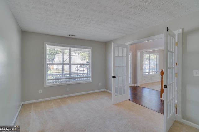 carpeted empty room with a textured ceiling and french doors