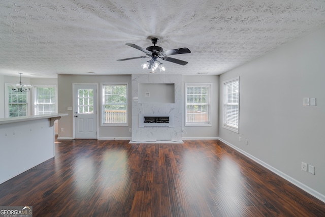 unfurnished living room featuring ceiling fan with notable chandelier, a textured ceiling, a fireplace, and dark hardwood / wood-style floors