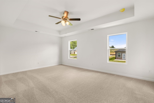 empty room featuring carpet floors, a raised ceiling, and ceiling fan