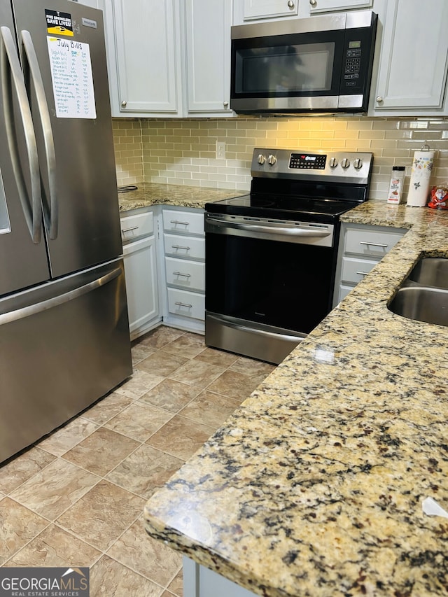 kitchen featuring light stone countertops, appliances with stainless steel finishes, white cabinets, and tasteful backsplash