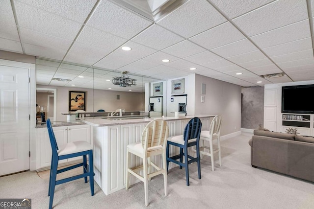 bar with light colored carpet, a paneled ceiling, and white cabinets