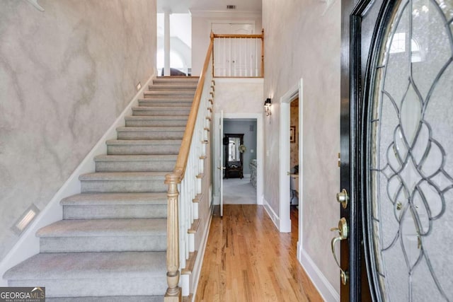 foyer entrance with light hardwood / wood-style flooring, a towering ceiling, and crown molding