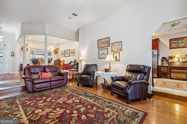 living room featuring wood-type flooring, ceiling fan with notable chandelier, decorative columns, and ornamental molding