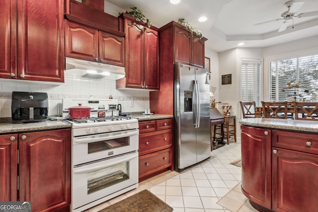 kitchen with a tray ceiling, tasteful backsplash, white range with gas stovetop, ceiling fan, and stainless steel fridge